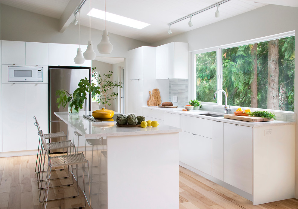 This is an example of a mid-sized contemporary kitchen in Vancouver with a single-bowl sink, flat-panel cabinets, white cabinets, grey splashback, stainless steel appliances, light hardwood floors and with island.