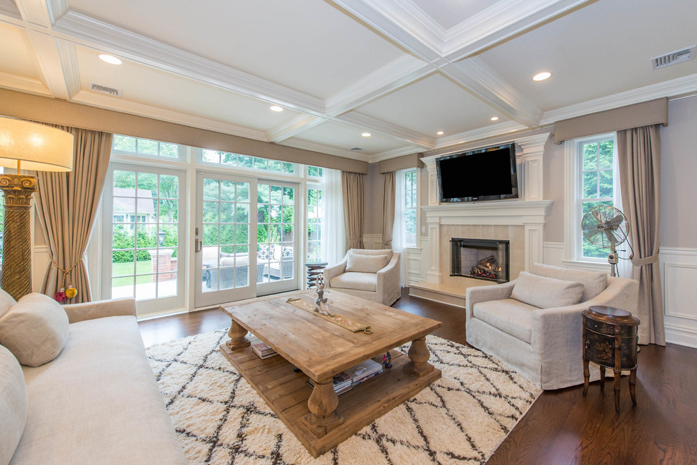 Large traditional open concept family room in New York with grey walls, medium hardwood floors, a wood fireplace surround and a wall-mounted tv.