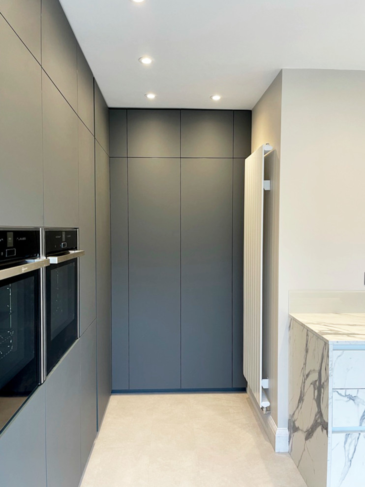 Medium sized modern grey and white l-shaped kitchen/diner in London with an integrated sink, flat-panel cabinets, green cabinets, laminate countertops, white splashback, glass sheet splashback, black appliances, laminate floors, no island, beige floors, white worktops and feature lighting.