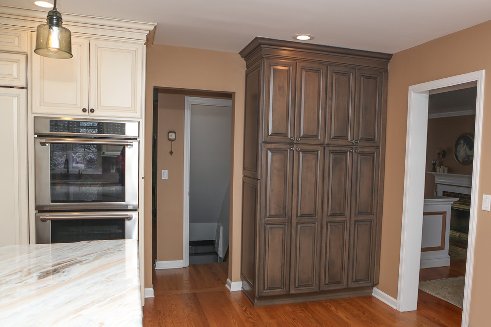 Eat-in kitchen - large transitional u-shaped light wood floor eat-in kitchen idea in Newark with an undermount sink, raised-panel cabinets, distressed cabinets, granite countertops, brown backsplash, mosaic tile backsplash, stainless steel appliances and an island
