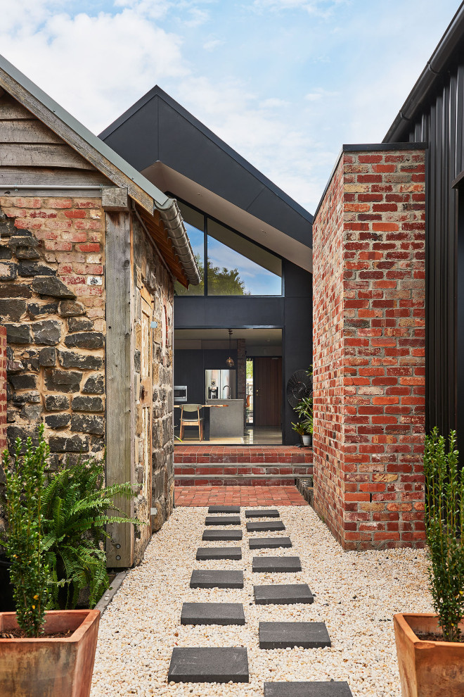 This is an example of a mid-sized contemporary one-storey brick red house exterior in Geelong with a gable roof, a metal roof and a black roof.