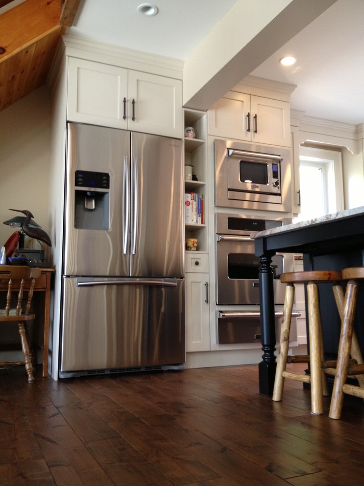 Example of a mid-sized transitional l-shaped medium tone wood floor eat-in kitchen design in Toronto with a double-bowl sink, shaker cabinets, white cabinets, stainless steel appliances, an island and granite countertops