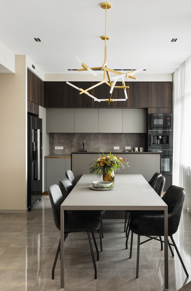 This is an example of a mid-sized contemporary l-shaped eat-in kitchen in Saint Petersburg with flat-panel cabinets, grey cabinets, grey splashback, porcelain splashback, black appliances, porcelain floors, grey floor, grey benchtop, a drop-in sink and with island.