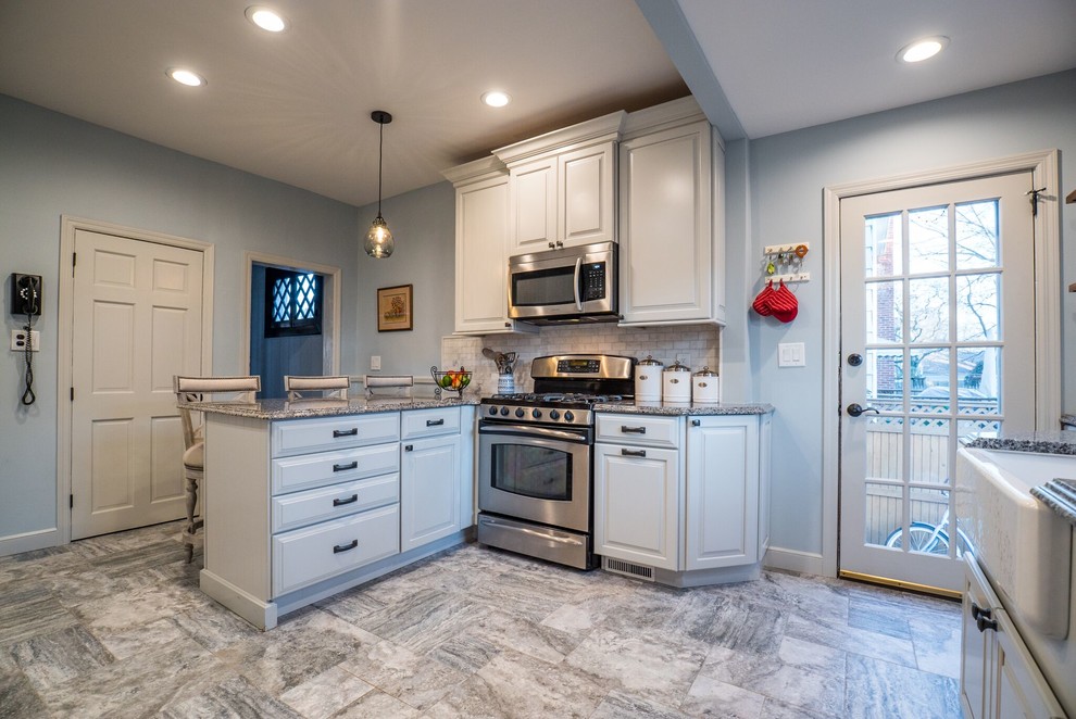 Mid-sized traditional u-shaped eat-in kitchen in Other with a farmhouse sink, raised-panel cabinets, white cabinets, granite benchtops, grey splashback, marble splashback, stainless steel appliances, porcelain floors, grey floor, blue benchtop and a peninsula.