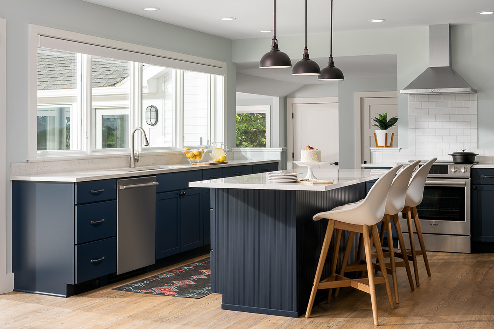Mid-sized transitional vinyl floor and brown floor kitchen photo in Burlington with an undermount sink, flat-panel cabinets, blue cabinets, quartz countertops, white backsplash, stainless steel appliances, an island, subway tile backsplash and white countertops