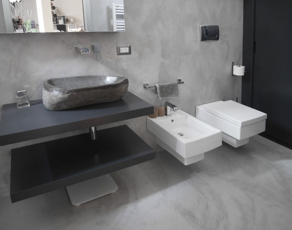 Mid-sized contemporary 3/4 bathroom in Milan with flat-panel cabinets, grey cabinets, an alcove shower, a wall-mount toilet, gray tile, grey walls, concrete floors, a vessel sink, wood benchtops, grey floor, a sliding shower screen and grey benchtops.