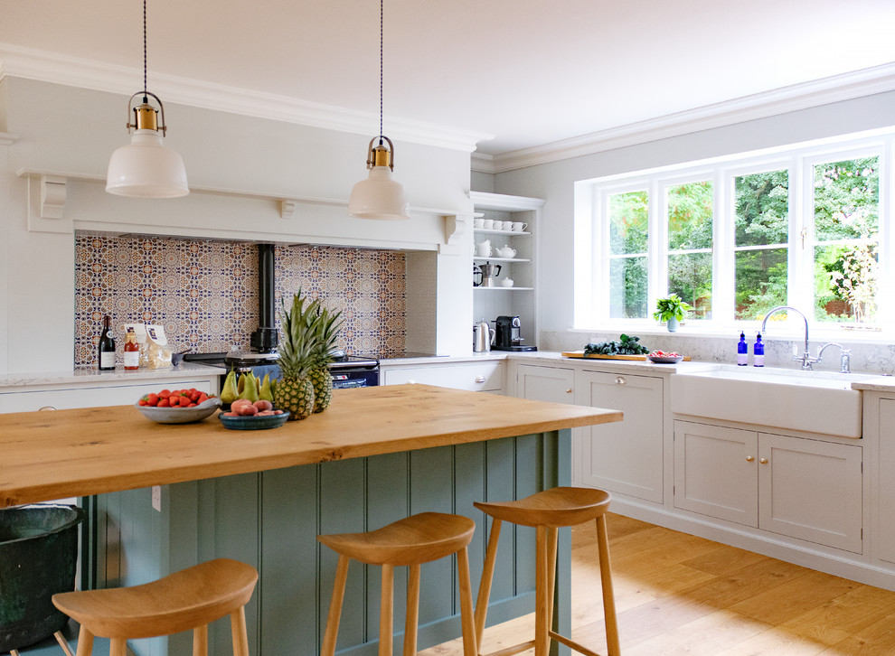 Design ideas for a large transitional u-shaped eat-in kitchen in Hertfordshire with shaker cabinets, white cabinets, quartz benchtops, stainless steel appliances, medium hardwood floors, with island, brown floor, grey benchtop, a farmhouse sink, multi-coloured splashback and cement tile splashback.
