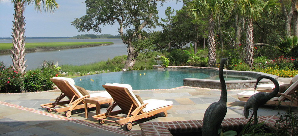 This is an example of a large tropical backyard round aboveground pool in Charleston with a hot tub and brick pavers.