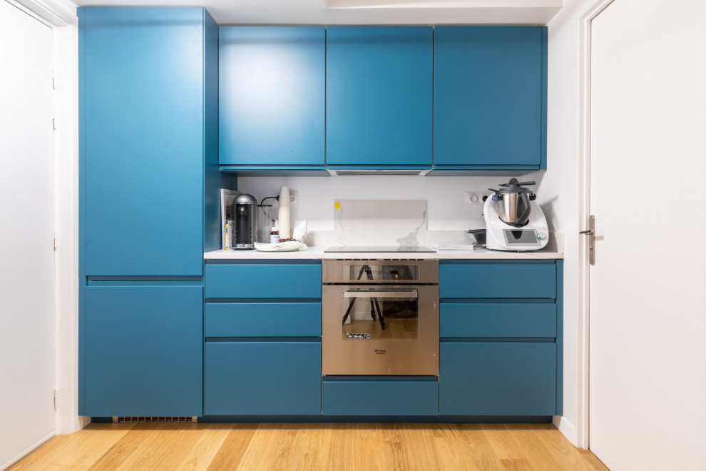 Design ideas for a small contemporary l-shaped separate kitchen in Paris with a single-bowl sink, blue cabinets, stainless steel appliances, light hardwood floors, no island, brown floor and white benchtop.