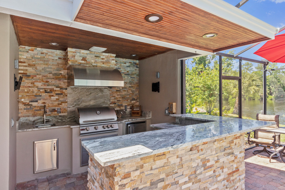 Inspiration for a contemporary patio in Orlando with an outdoor kitchen, natural stone pavers and a roof extension.
