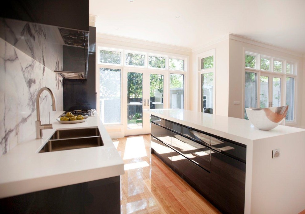 Mid-sized contemporary single-wall open plan kitchen in Melbourne with a double-bowl sink, flat-panel cabinets, black cabinets, quartz benchtops, multi-coloured splashback, marble splashback, stainless steel appliances, medium hardwood floors and with island.