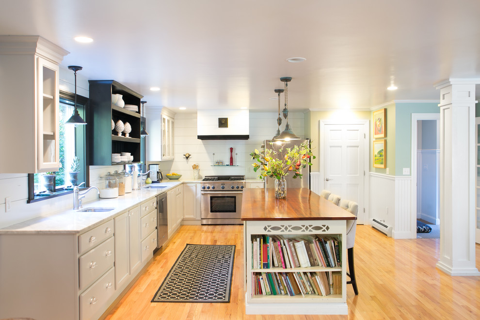 Design ideas for a transitional l-shaped kitchen in Portland Maine with an undermount sink, recessed-panel cabinets, beige cabinets, white splashback, stainless steel appliances and wood benchtops.