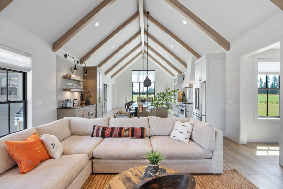 Design ideas for an expansive country open concept living room in Portland with a library, white walls, vinyl floors, a standard fireplace, a plaster fireplace surround, a freestanding tv, brown floor and exposed beam.