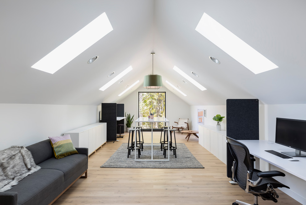 Skandinavisk inredning av ett stort hemmastudio, med vita väggar, ljust trägolv, ett fristående skrivbord och beiget golv