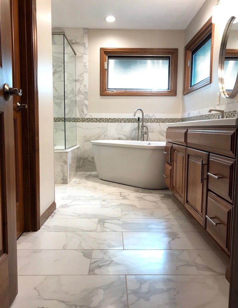 Inspiration for a mid-sized transitional master gray tile and porcelain tile porcelain tile and gray floor freestanding bathtub remodel with raised-panel cabinets, medium tone wood cabinets, beige walls, an integrated sink, white countertops, solid surface countertops and a hinged shower door