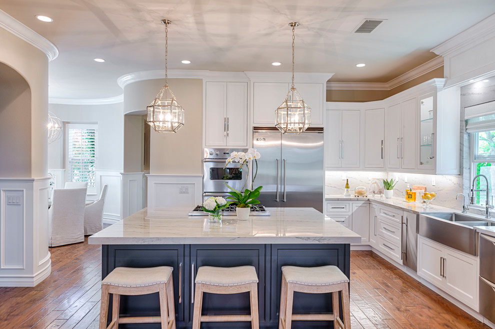 Example of a large transitional l-shaped medium tone wood floor eat-in kitchen design in Orange County with a drop-in sink, quartzite countertops, white backsplash, stone slab backsplash, stainless steel appliances, an island, beaded inset cabinets and white cabinets