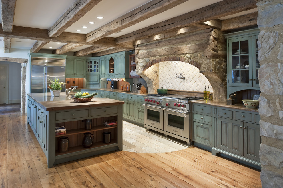 Large country l-shaped eat-in kitchen in Philadelphia with stainless steel appliances, raised-panel cabinets, distressed cabinets, white splashback, porcelain splashback, light hardwood floors, with island, brown floor, a farmhouse sink, granite benchtops and brown benchtop.