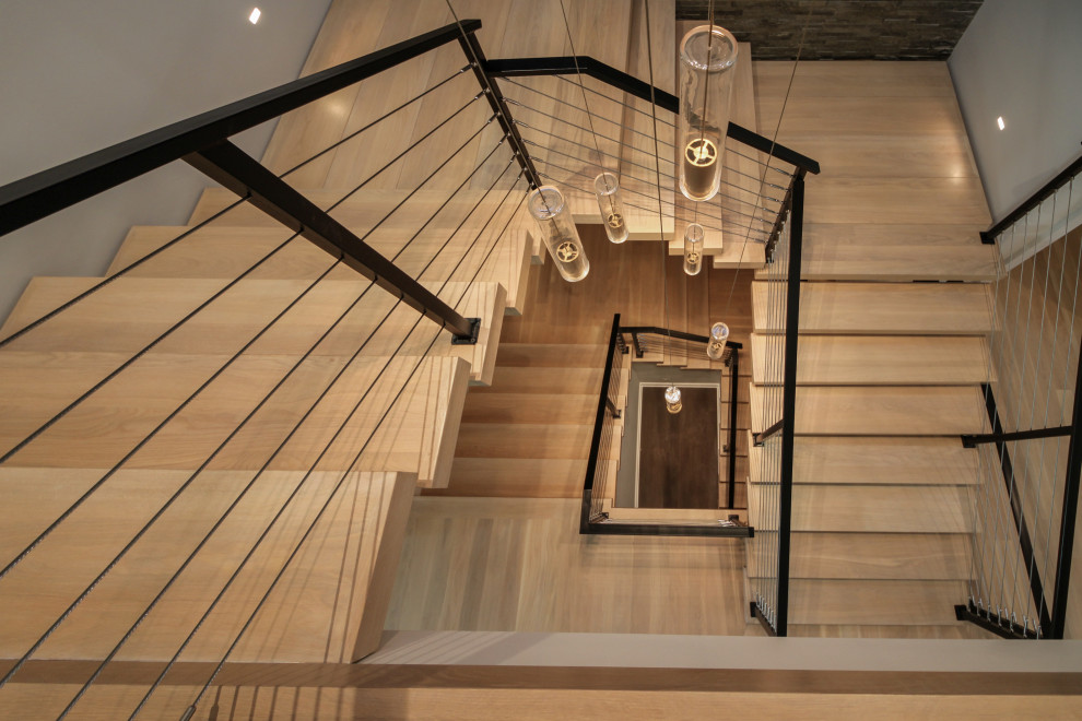 Exemple d'un grand escalier flottant éclectique avec des marches en bois, un garde-corps en métal et un mur en parement de brique.