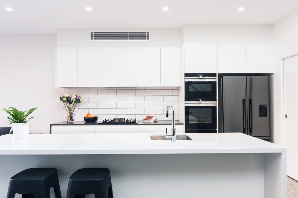Inspiration for a contemporary galley open plan kitchen in Sydney with an undermount sink, flat-panel cabinets, white cabinets, quartz benchtops, white splashback, subway tile splashback, stainless steel appliances, concrete floors, with island and white benchtop.