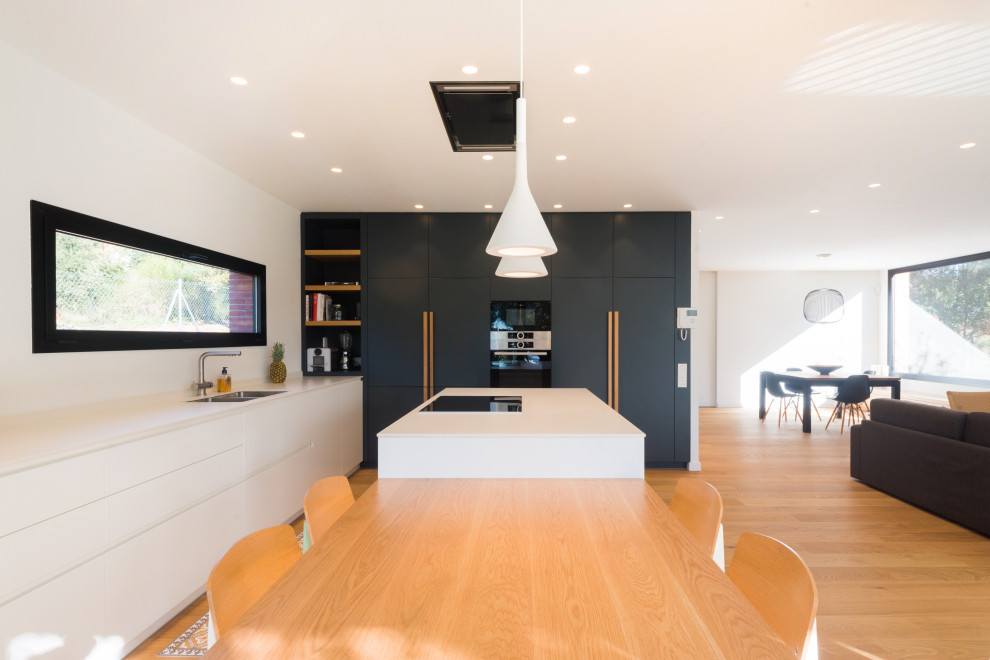 Large contemporary l-shaped open plan kitchen in Barcelona with flat-panel cabinets, quartz benchtops, panelled appliances, medium hardwood floors, with island, white benchtop, an undermount sink, white cabinets and beige floor.