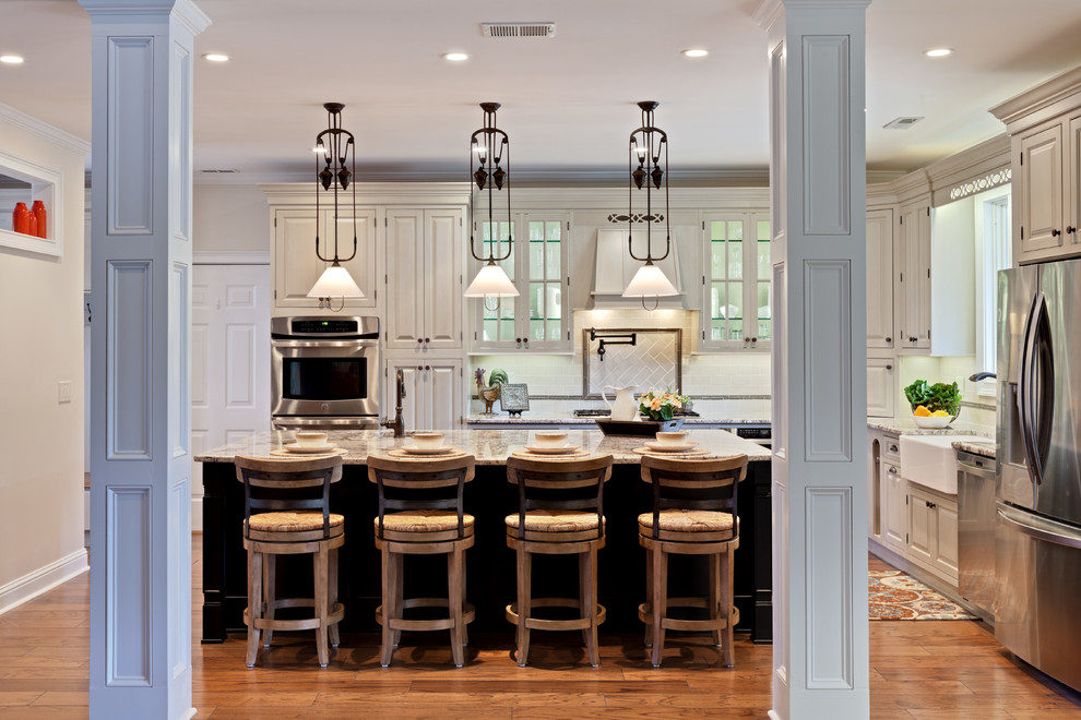 This is an example of an expansive traditional l-shaped eat-in kitchen in Atlanta with a farmhouse sink, beaded inset cabinets, beige cabinets, granite benchtops, beige splashback, porcelain splashback, stainless steel appliances, medium hardwood floors, with island, brown floor and beige benchtop.