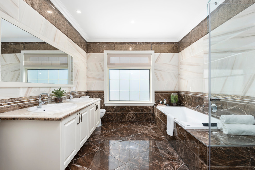 Стильный дизайн: большая главная ванная комната в классическом стиле с фасадами с утопленной филенкой, бежевыми фасадами, гидромассажной ванной, душем без бортиков, раздельным унитазом, коричневой плиткой, керамической плиткой, бежевыми стенами, полом из керамической плитки, накладной раковиной, мраморной столешницей, коричневым полом, душем с распашными дверями, бежевой столешницей, тумбой под две раковины и подвесной тумбой - последний тренд