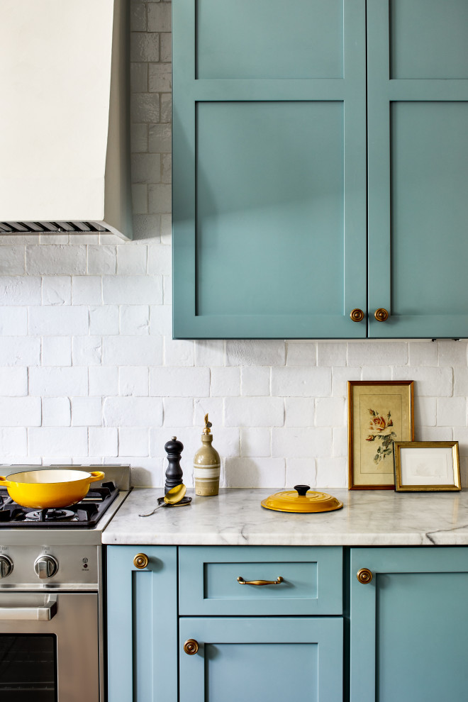 Exemple d'une grande cuisine américaine chic avec un placard à porte shaker, des portes de placard bleues, plan de travail en marbre et une crédence blanche.