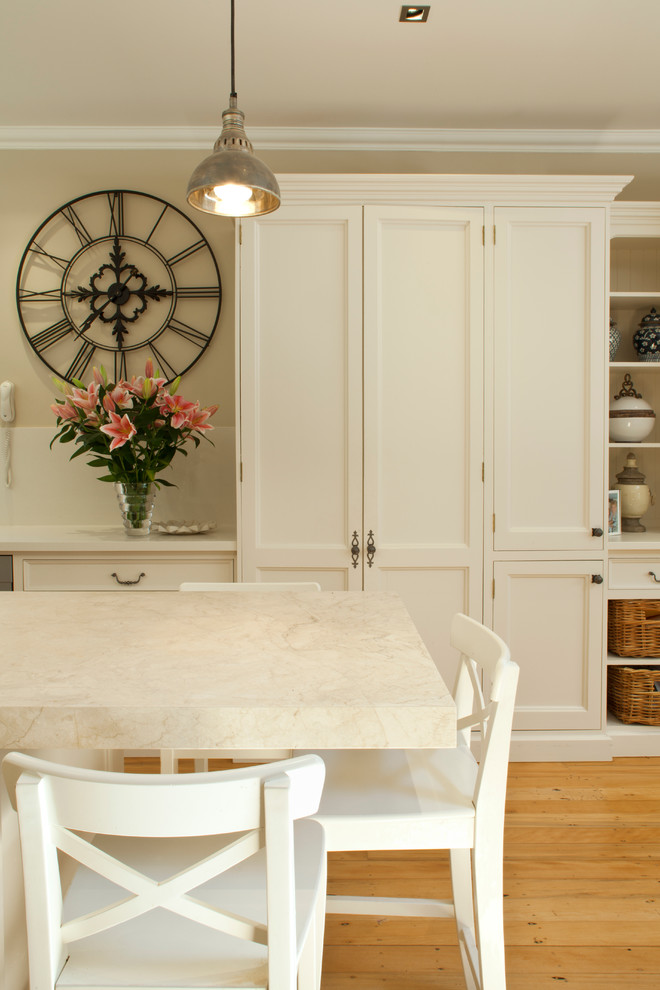 This is an example of a large transitional u-shaped open plan kitchen in Sydney with a farmhouse sink, shaker cabinets, white cabinets, limestone benchtops, white splashback, glass sheet splashback, stainless steel appliances, medium hardwood floors and with island.