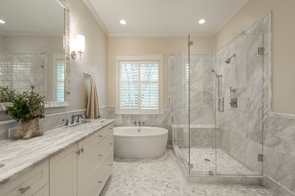 Photo of a large transitional master bathroom in Dallas with shaker cabinets, white cabinets, a freestanding tub, a corner shower, a one-piece toilet, gray tile, stone tile, grey walls, mosaic tile floors, an undermount sink and marble benchtops.