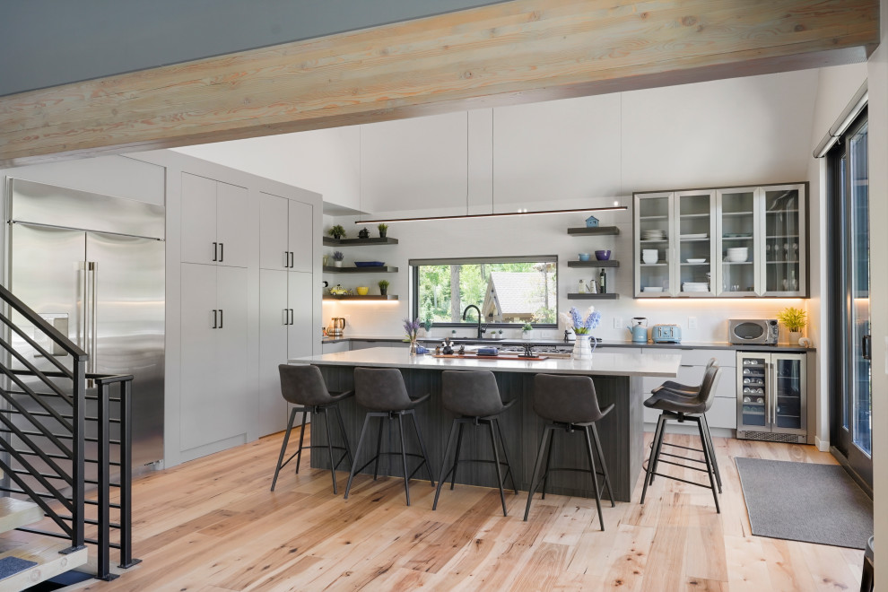 This is an example of a large contemporary l-shaped open plan kitchen in Denver with a submerged sink, flat-panel cabinets, grey cabinets, white splashback, stainless steel appliances, an island and a vaulted ceiling.