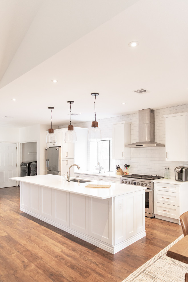 Mid-sized transitional medium tone wood floor and brown floor eat-in kitchen photo in Phoenix with shaker cabinets, white cabinets, white backsplash, subway tile backsplash, stainless steel appliances and an island