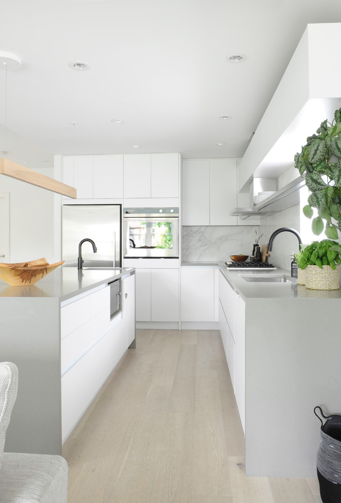 Photo of a mid-sized scandinavian open plan kitchen in Vancouver with flat-panel cabinets, white cabinets, quartz benchtops, stone slab splashback, light hardwood floors, with island and grey benchtop.