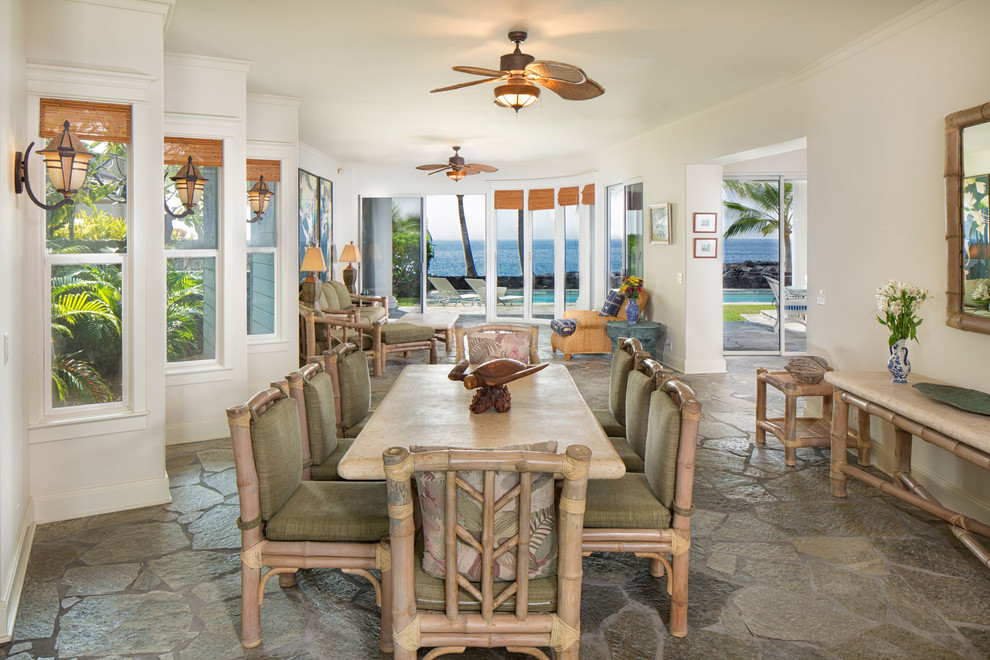 Large beach style dining room in Hawaii with white walls and limestone floors.