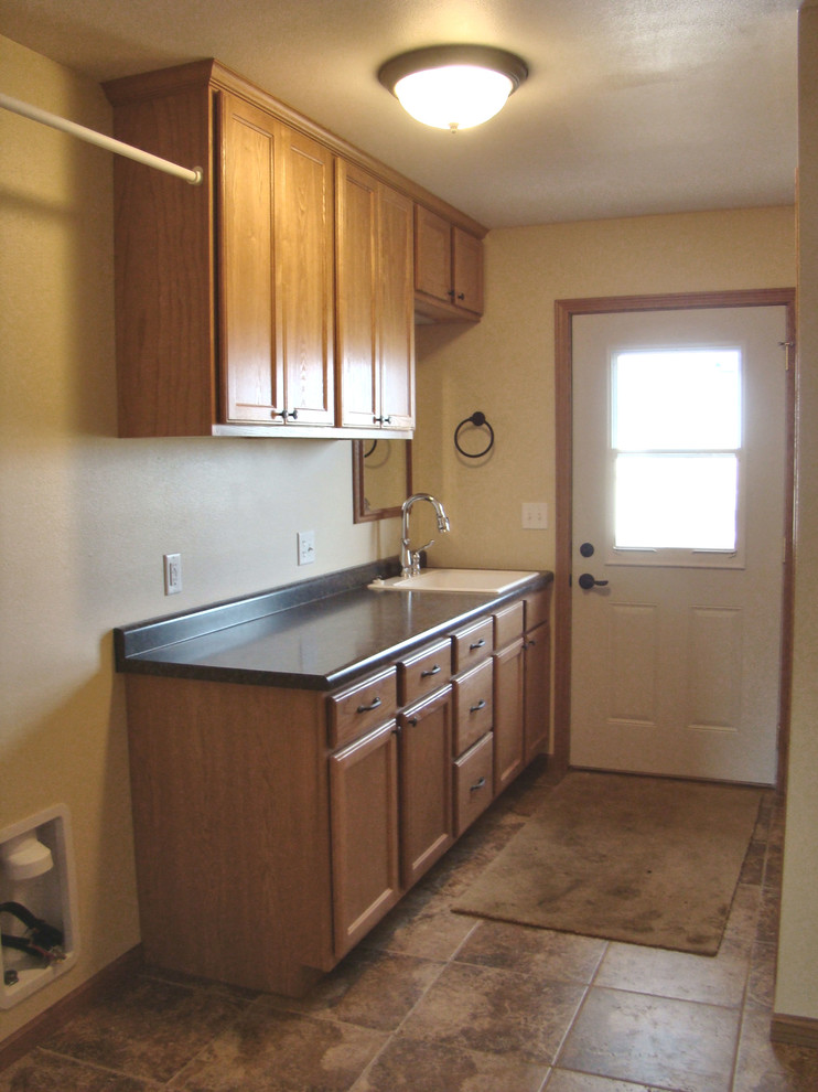 This is an example of a mid-sized transitional galley utility room in Other with a drop-in sink, shaker cabinets, brown cabinets, laminate benchtops, yellow walls, ceramic floors, a side-by-side washer and dryer, brown floor and black benchtop.