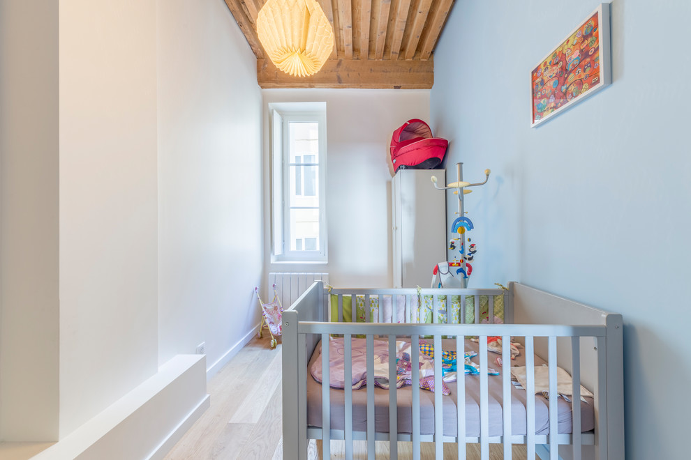 Réalisation de chambre de bébé fille pour fille avec un mur bleu, parquet clair et un sol beige.