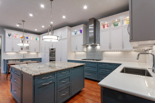 Two-tone kitchen with white uppers and blue shaker RTA cabinets, large granite island, stainless range hood, and under-cabinet lighting.