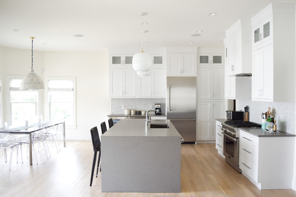 Mid-sized transitional l-shaped eat-in kitchen in New York with an undermount sink, recessed-panel cabinets, white cabinets, quartz benchtops, grey splashback, marble splashback, stainless steel appliances, light hardwood floors, with island and beige floor.