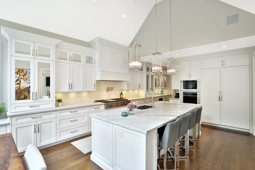 Large transitional l-shaped kitchen pantry in Toronto with an undermount sink, shaker cabinets, white cabinets, quartz benchtops, white splashback, marble splashback, panelled appliances, medium hardwood floors, with island, brown floor and white benchtop.