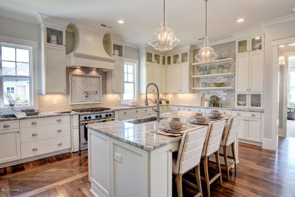This is an example of an expansive transitional u-shaped kitchen pantry in Other with a farmhouse sink, shaker cabinets, white cabinets, quartz benchtops, beige splashback, ceramic splashback, stainless steel appliances, medium hardwood floors, with island and brown floor.