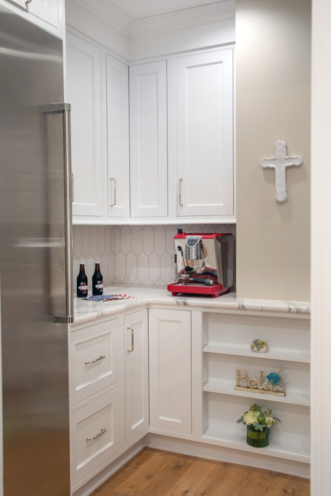 This is an example of a mid-sized transitional l-shaped separate kitchen in Milwaukee with an undermount sink, beaded inset cabinets, white cabinets, quartz benchtops, white splashback, cement tile splashback, white appliances, light hardwood floors, with island, brown floor, white benchtop and timber.