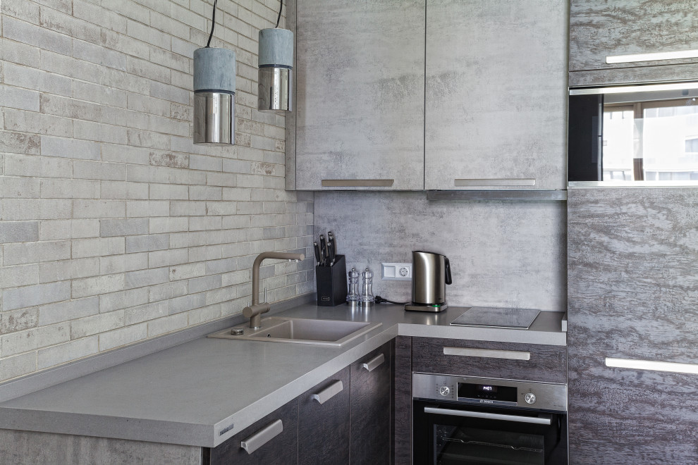 Small industrial l-shaped eat-in kitchen in Other with a single-bowl sink, flat-panel cabinets, quartz benchtops, brick splashback, stainless steel appliances, porcelain floors, no island, grey floor, grey benchtop and exposed beam.