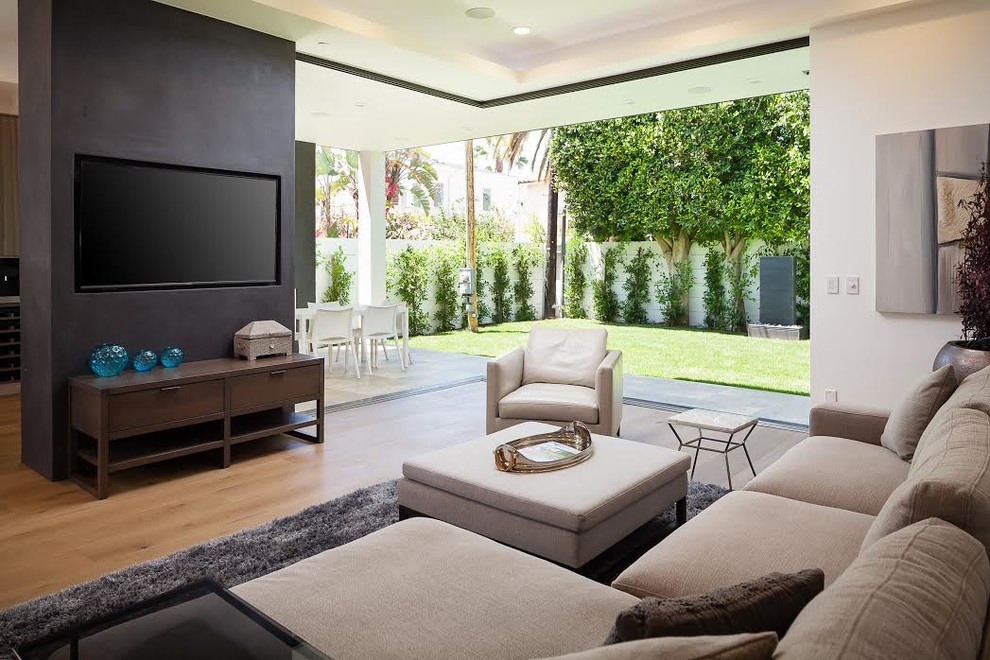 This is an example of a contemporary family room in Los Angeles with white walls, medium hardwood floors and a wall-mounted tv.