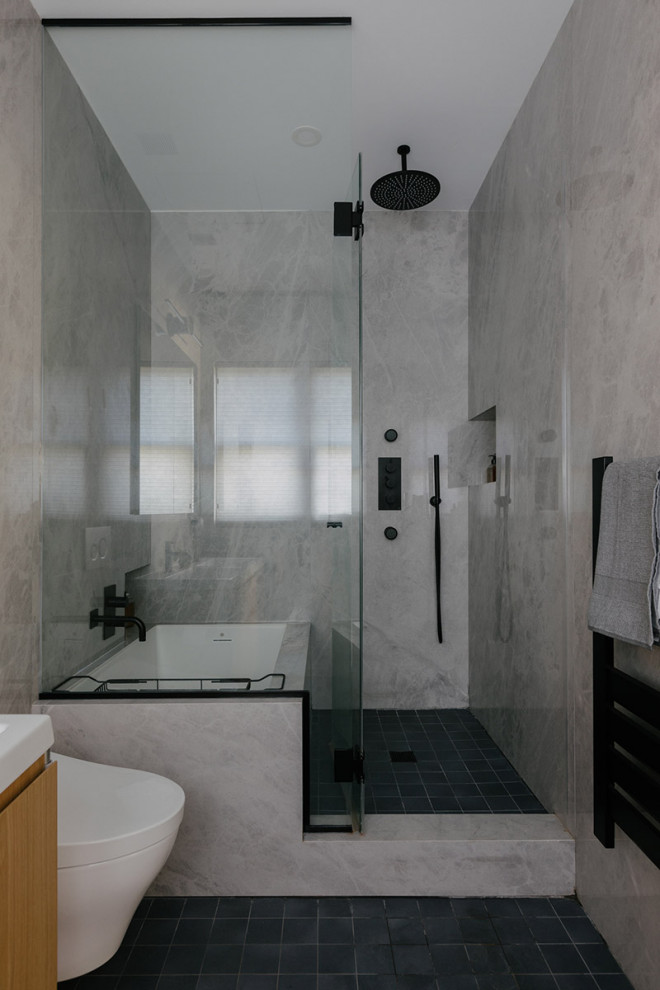 Photo of a mid-sized modern master bathroom in New York with flat-panel cabinets, brown cabinets, a shower/bathtub combo, a wall-mount toilet, gray tile, stone slab, grey walls, porcelain floors, an integrated sink, solid surface benchtops, blue floor, an open shower, white benchtops, a double vanity, a floating vanity and panelled walls.