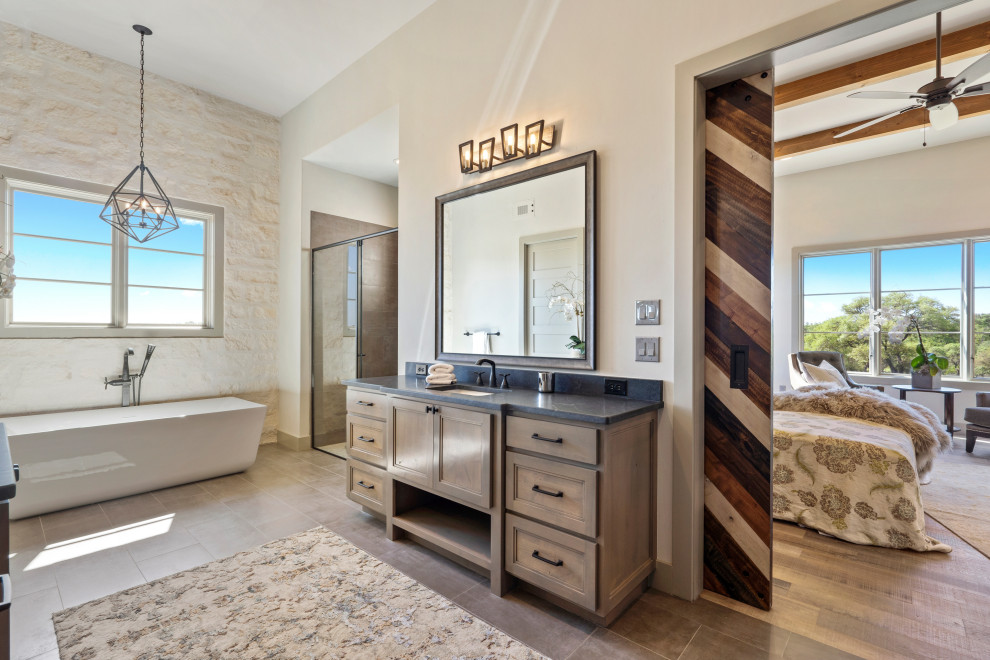 Photo of a large country master bathroom in Austin with shaker cabinets, grey cabinets, a freestanding tub, a curbless shower, a two-piece toilet, grey walls, porcelain floors, an undermount sink, granite benchtops, grey floor, a hinged shower door, black benchtops, an enclosed toilet, a double vanity and a built-in vanity.