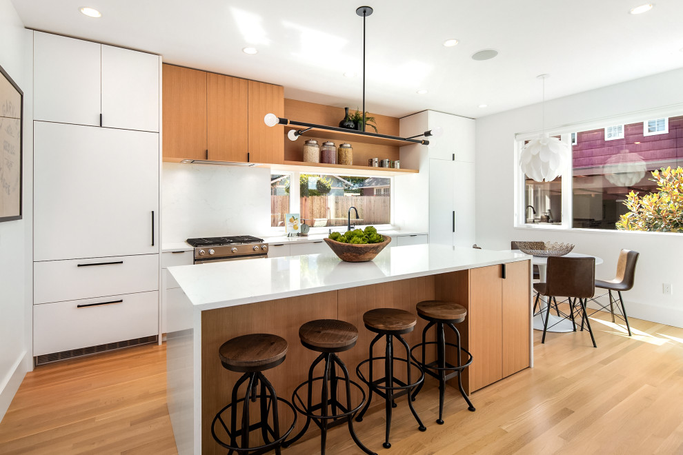 Design ideas for a mid-sized contemporary single-wall eat-in kitchen in Seattle with flat-panel cabinets, white cabinets, quartz benchtops, white splashback, engineered quartz splashback, stainless steel appliances, light hardwood floors, with island and white benchtop.