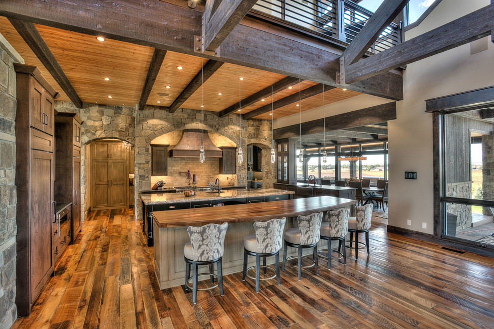 Example of a huge mountain style l-shaped medium tone wood floor eat-in kitchen design in Denver with an undermount sink, shaker cabinets, medium tone wood cabinets, granite countertops, beige backsplash, stone tile backsplash, stainless steel appliances and two islands
