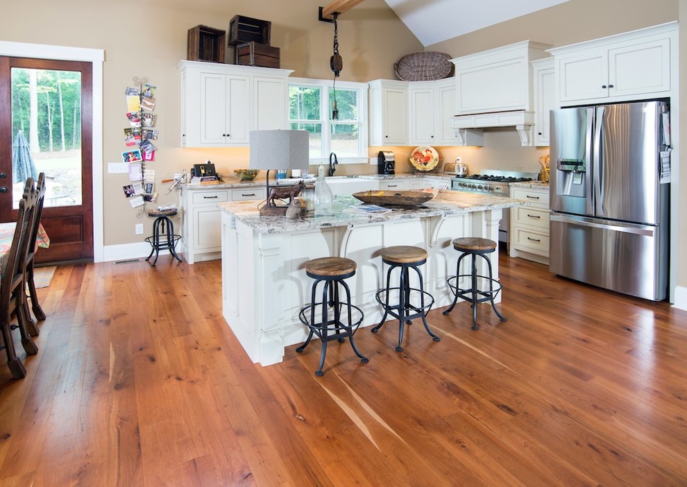 Mid-sized country l-shaped open plan kitchen in Atlanta with a farmhouse sink, shaker cabinets, white cabinets, granite benchtops, beige splashback, stainless steel appliances, medium hardwood floors, with island and brown floor.