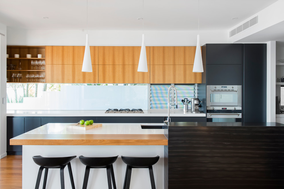 Photo of a contemporary galley open plan kitchen in Brisbane with an undermount sink, flat-panel cabinets, light wood cabinets, glass sheet splashback, stainless steel appliances, light hardwood floors and with island.