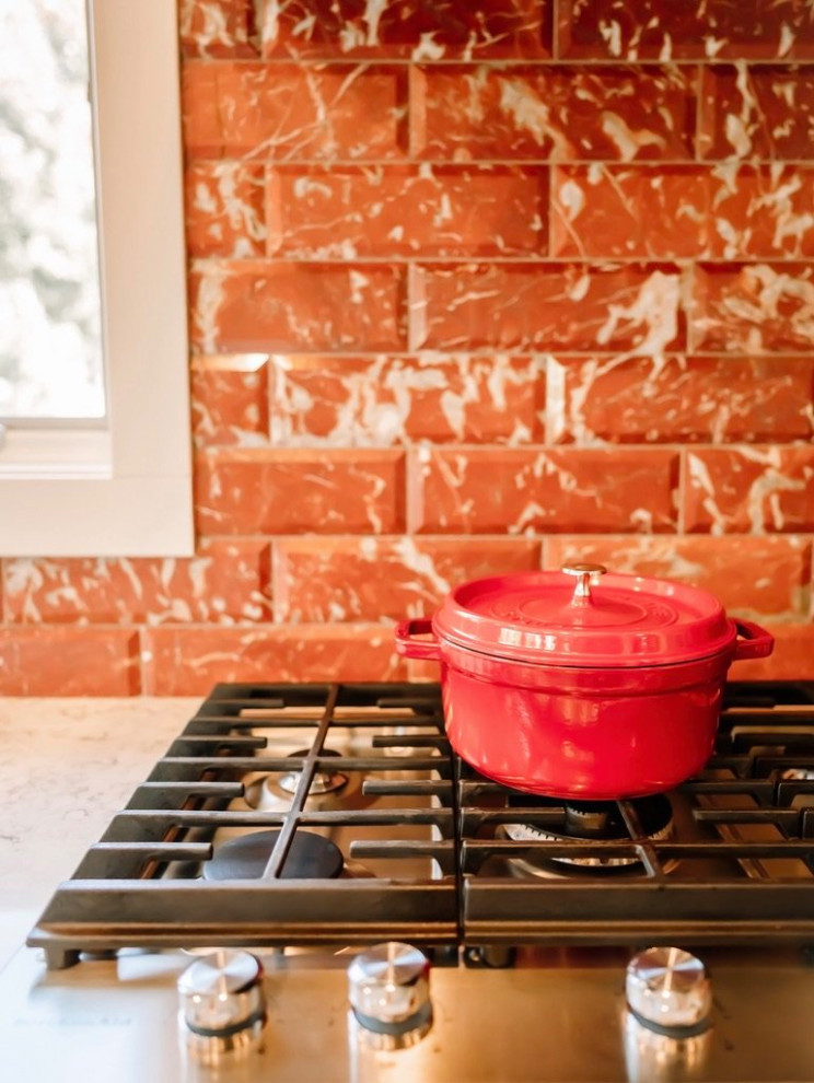 シーダーラピッズにある高級なコンテンポラリースタイルのおしゃれなキッチン (御影石カウンター、シルバーの調理設備、白いキッチンカウンター、赤いキッチンパネル、サブウェイタイルのキッチンパネル) の写真