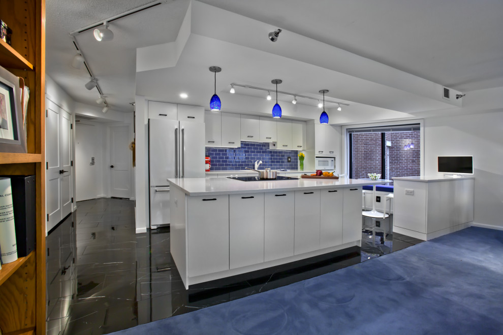 Mid-sized transitional single-wall open plan kitchen in Minneapolis with an undermount sink, flat-panel cabinets, white cabinets, quartz benchtops, blue splashback, ceramic splashback, white appliances, porcelain floors, with island, black floor and white benchtop.